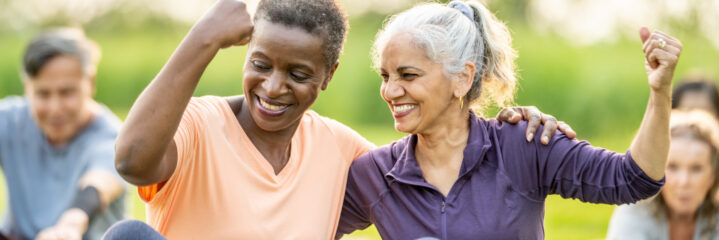Two senior women at outdoor exercise class smiling and flexing.